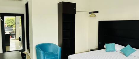 A modern hotel room with a large bed, a blue armchair, a black wardrobe, and a small table with a water bottle.