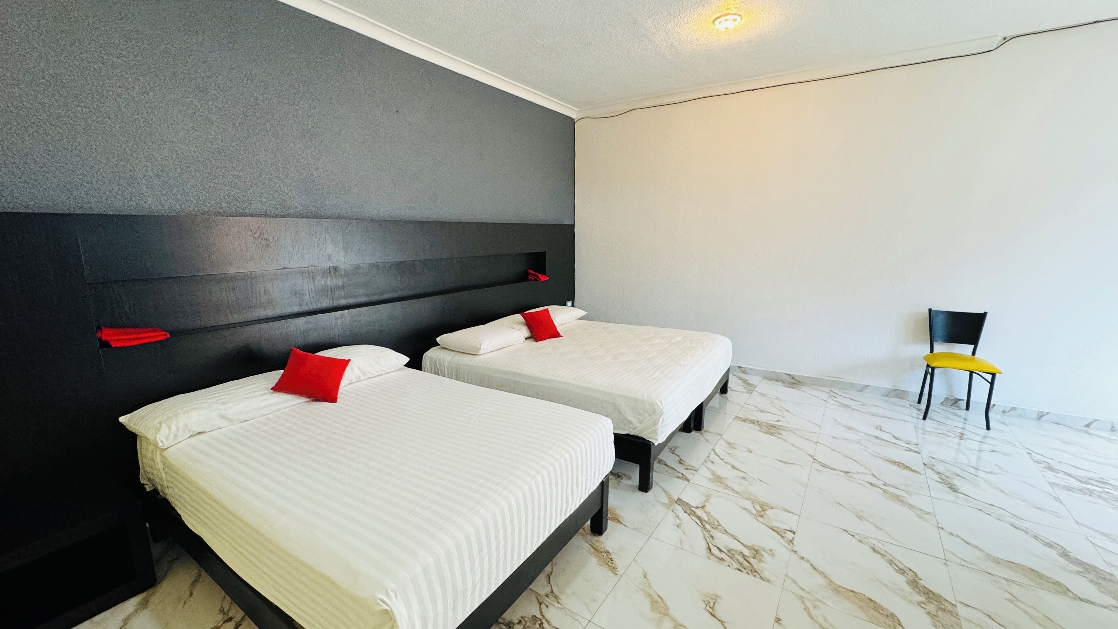 A hotel room with two beds, a black headboard, a chair, and a marble floor.
