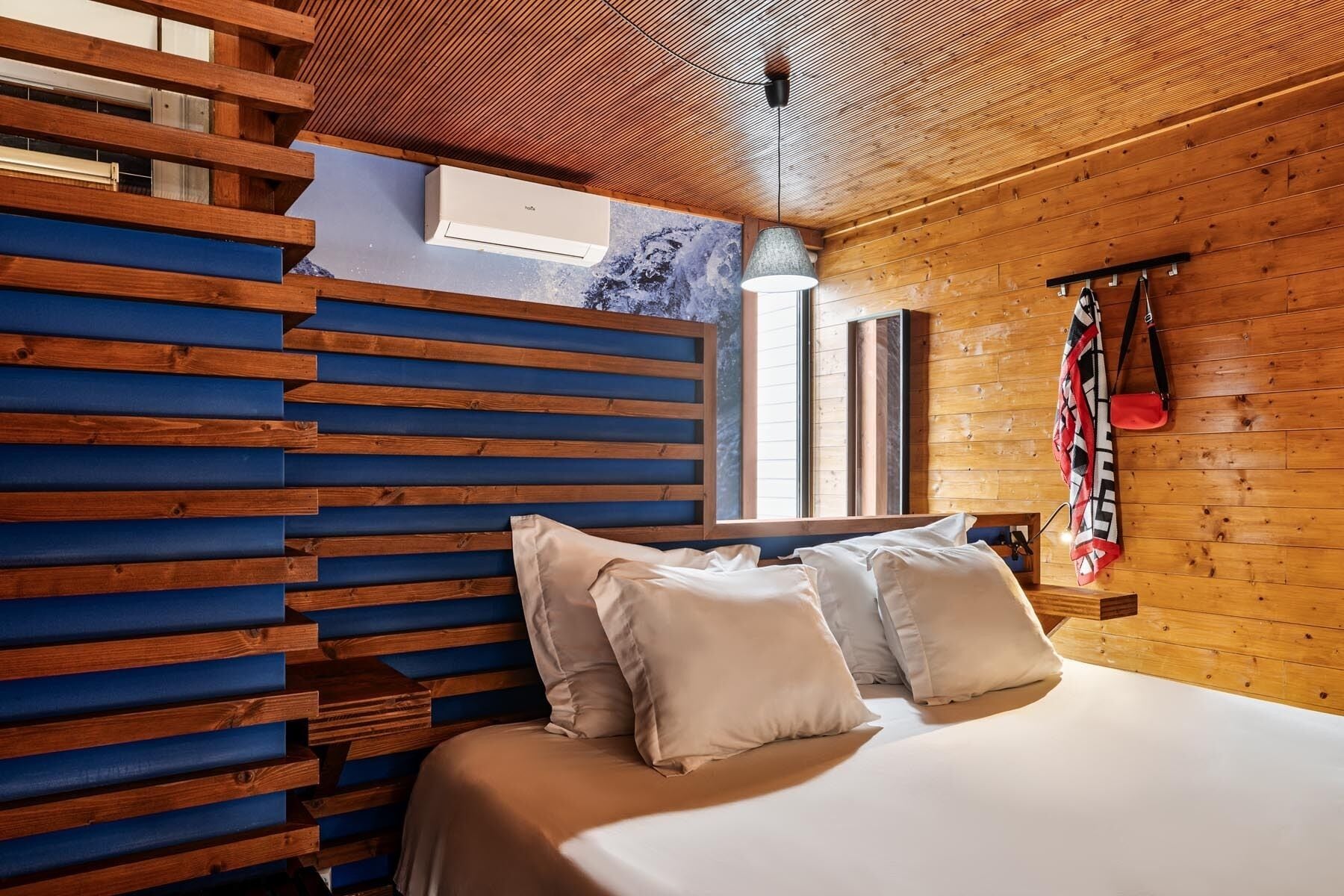 Un dormitorio con cabecera de madera con listones, cama con ropa blanca y una prenda colgada en la pared.