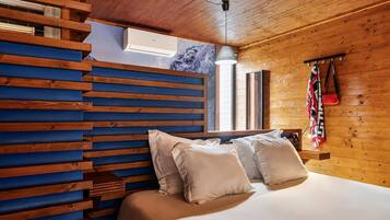 Quarto com cabeceira de madeira ripa, cama com roupa de cama branca e um cabide com roupa pendurada na parede.