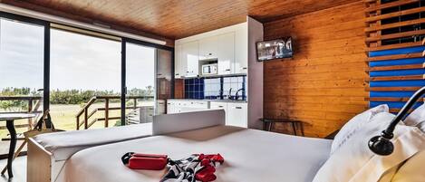 A modern bedroom with a large bed, a desk, and a kitchenette.