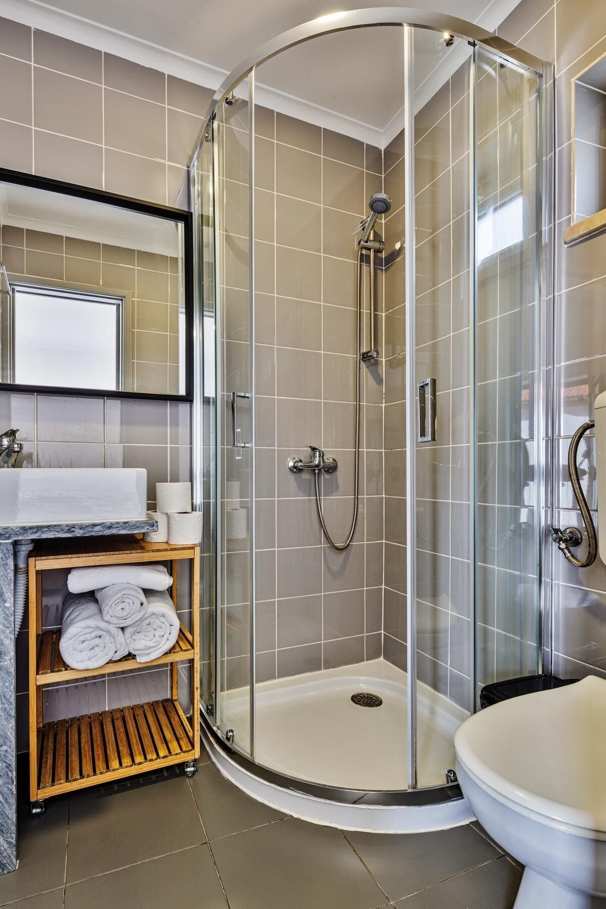 Un baño moderno con ducha envuelta en vidrio, un lavamanos con encimera de mármol y un inodoro.
