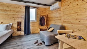 Ein gemütliches Zimmer mit Holzwänden, einem Bett, einem grauen Sofa, einem Tisch mit einer Zeitschrift und einem an der Wand befestigten Kleiderhaken.