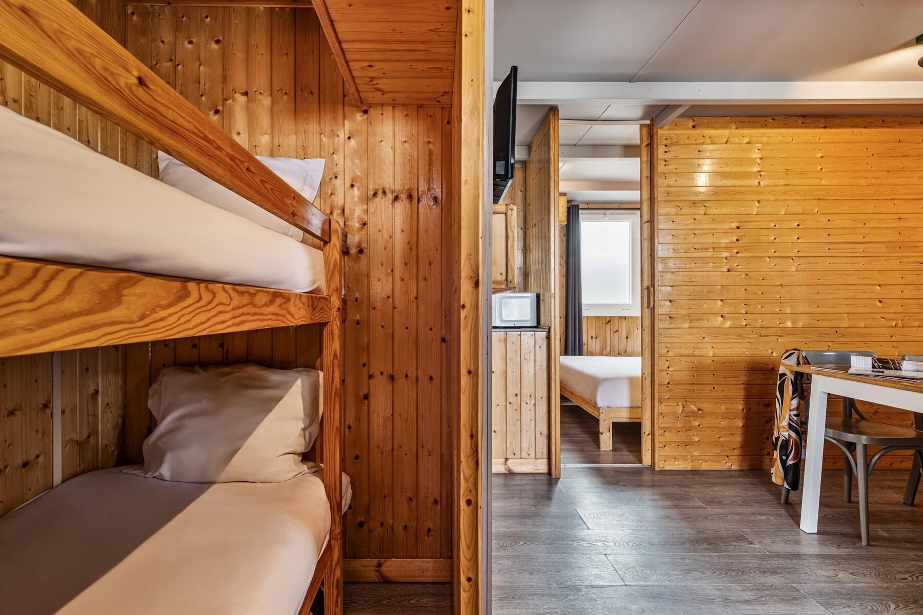 A bunk bed room with wooden walls, a small TV, and a table with a bag.