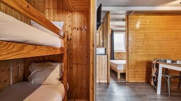 Habitación con literas, paredes de madera, un televisor pequeño y una mesa con un bolso.