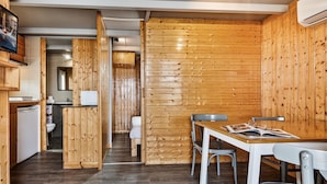 Ein kompakter Raum mit Holzwandverkleidung, einer kleinen Küchenzeile, einer Essecke mit Tisch und Stühlen sowie einer sichtbaren Toilette.