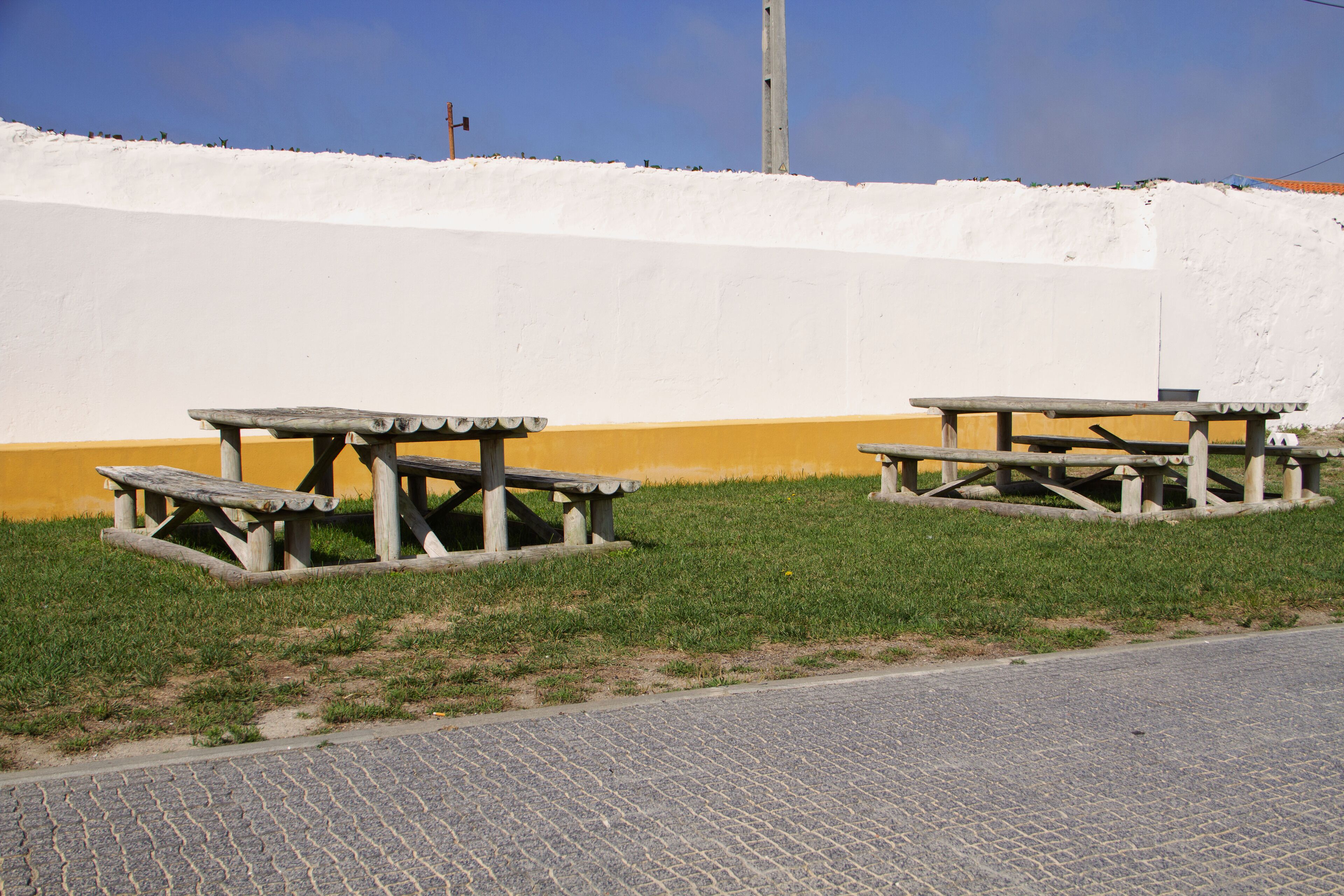 Two picnic tables with a white and yellow wall in the background.