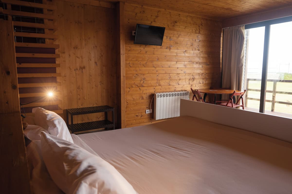 Ein Zimmer einer Holzhütte mit einem Bett, einem an der Wand befestigten Fernseher, einem kleinen Tisch und einem Stuhl.