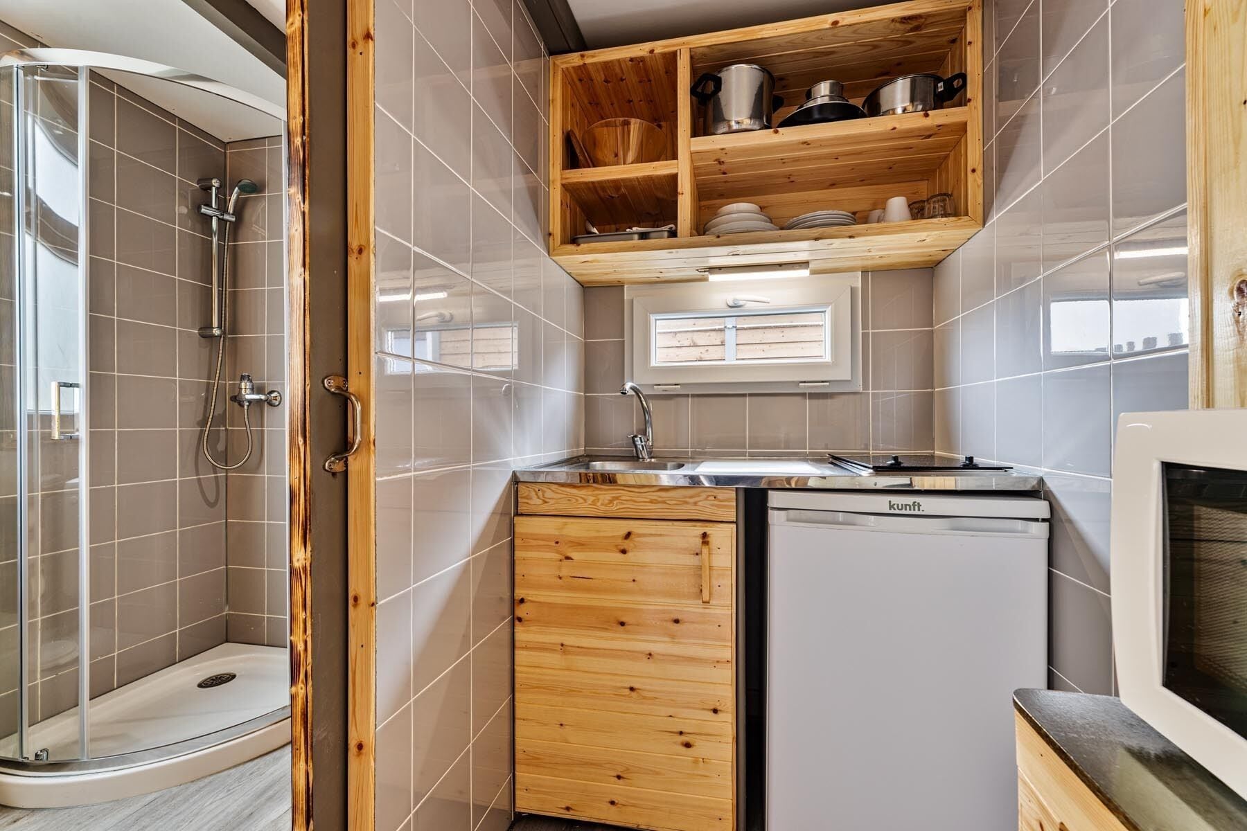 Una cocina compacta con lavavajillas integrado, armarios de madera y cabina de ducha con mampara de vidrio.