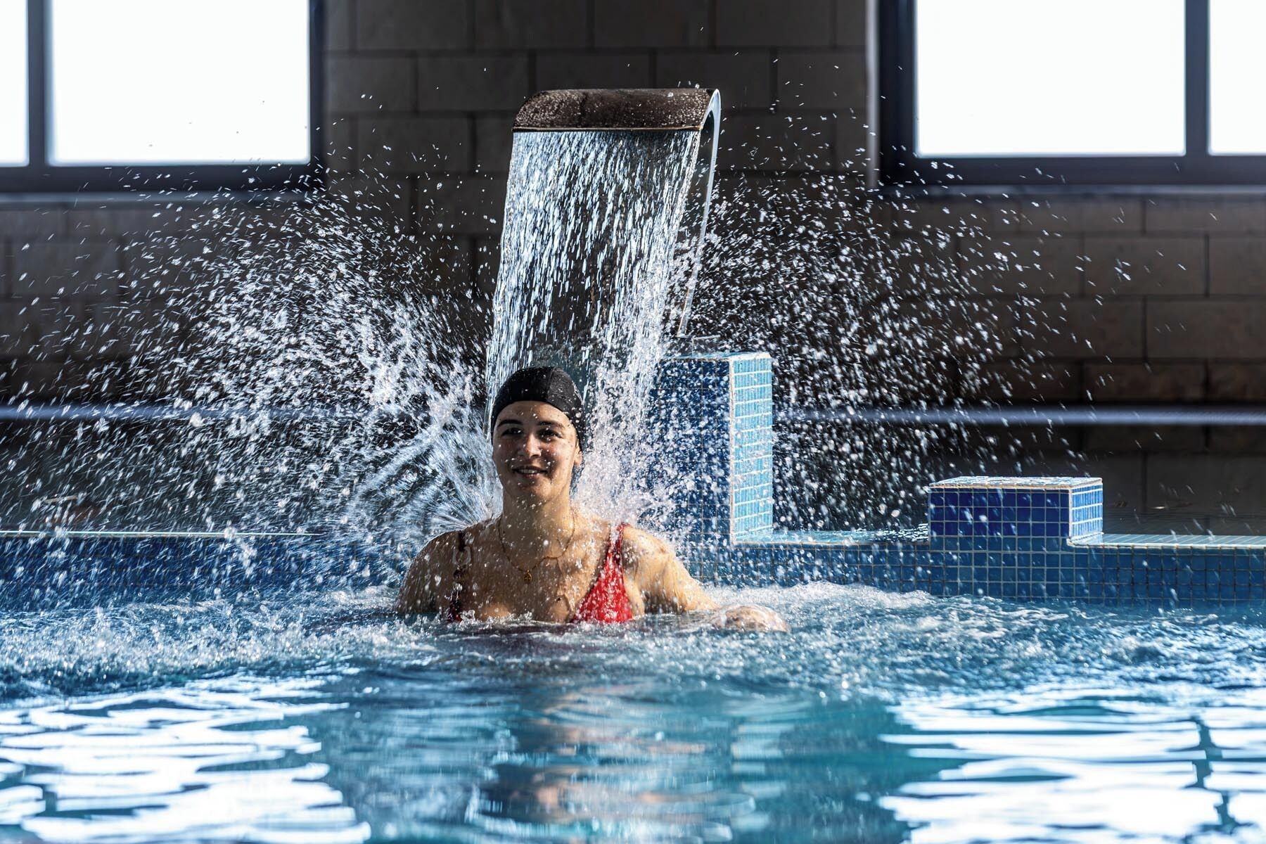 A person in a swimming pool with water cascading from a high wall.