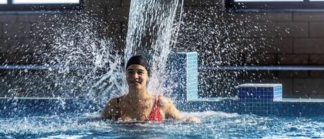 A person in a swimming pool with water cascading from a high wall.