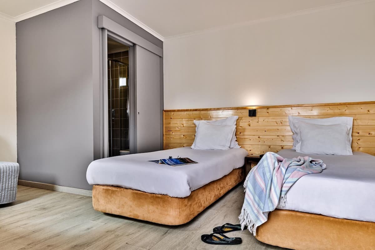 Ein Hotelzimmer mit zwei Betten, einem hölzernen Kopfteil, einer grauen Wand und einem Holzboden.