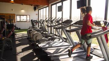 Un gimnasio con numerosas cintas de correr, máquinas de pesas y un amplio ventanal que proporciona luz natural.