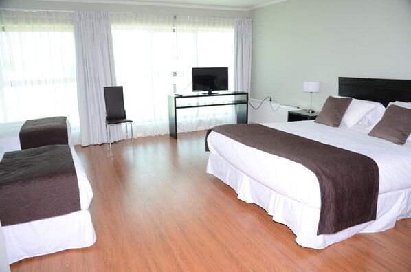 A hotel room with a large bed, a TV on a stand, a desk with a lamp, and a chair.
