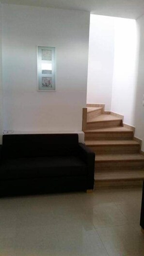 A living room with a black sofa, a staircase, and a framed picture on the wall. - Finiki Villas (Karpathos)