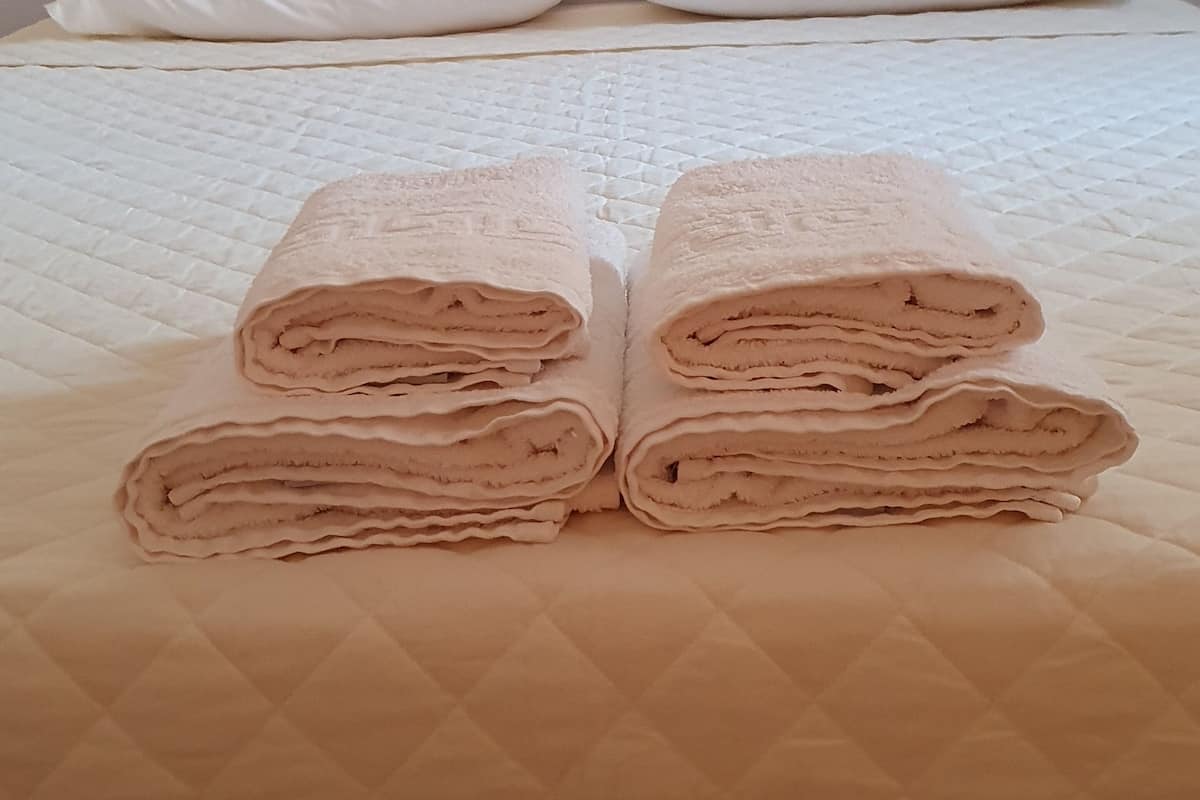 A neatly made bed with a quilted cover, two white pillows, and a folded towel stack.