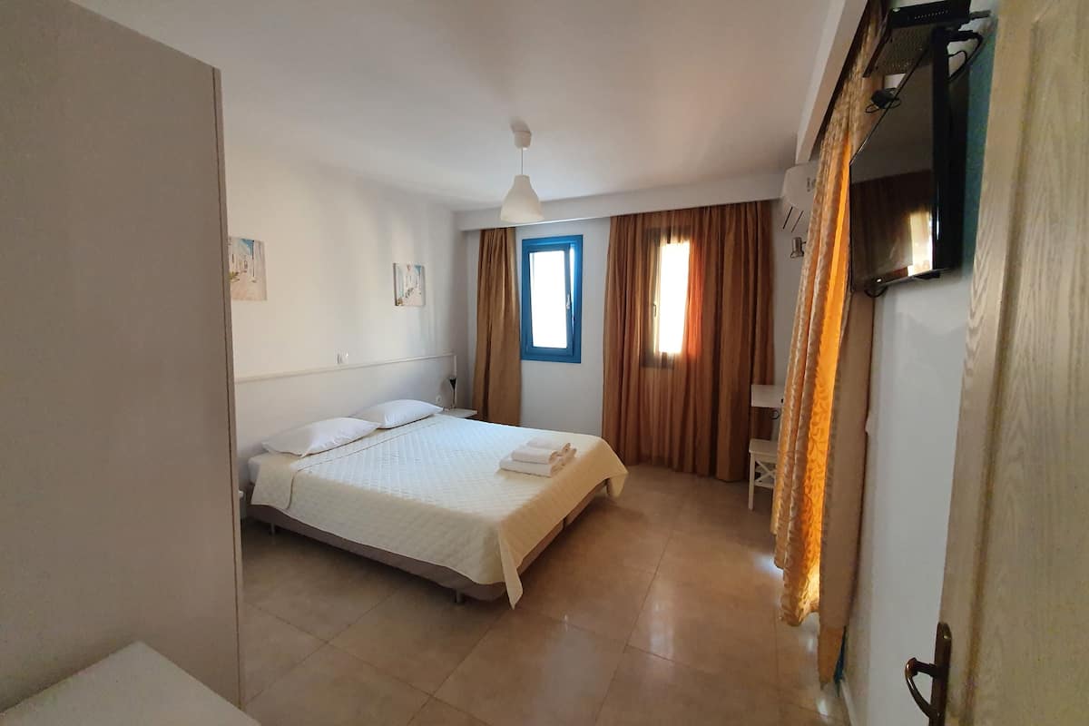 A bedroom with a bed, a window, a ceiling fan, and a TV mounted on the wall.