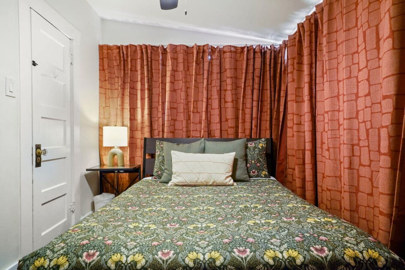 Une chambre à coucher avec une couvre-lit à motifs floraux, une lampe de chevet et un rideau à motifs.