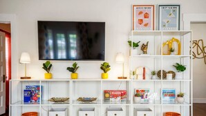 A living room with a TV, shelves with books, decorative items, and storage bins. - Bright and Quirky Hillcrest Craftsman (San Diego)