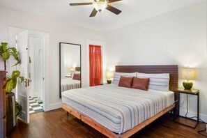 Un dormitorio con cama, ventilador de techo, mesita de noche, lámpara y espejo.