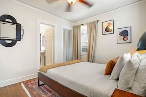 A bedroom with a bed, a ceiling fan, a window with curtains, and a wall-mounted mirror.