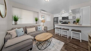 A modern living room with a sofa, coffee table, and kitchen area with bar stools. - Cozy & Chic 2br Retreat In Mission Beach (San Diego)