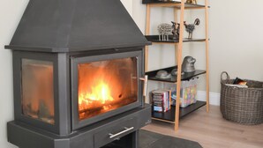 Uma lareira moderna com frente de vidro, uma estante de madeira com objetos decorativos e uma cesta de vime com livros.