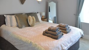 Uma cama bem arrumada com colcha estampada e várias almofadas. Uma decoração em formato de coração está pendurada na parede acima da cama.
