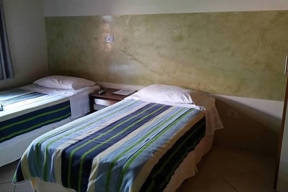 A room with two single beds, each with striped bedding. There is a small table between the beds, and a power outlet on the wall.