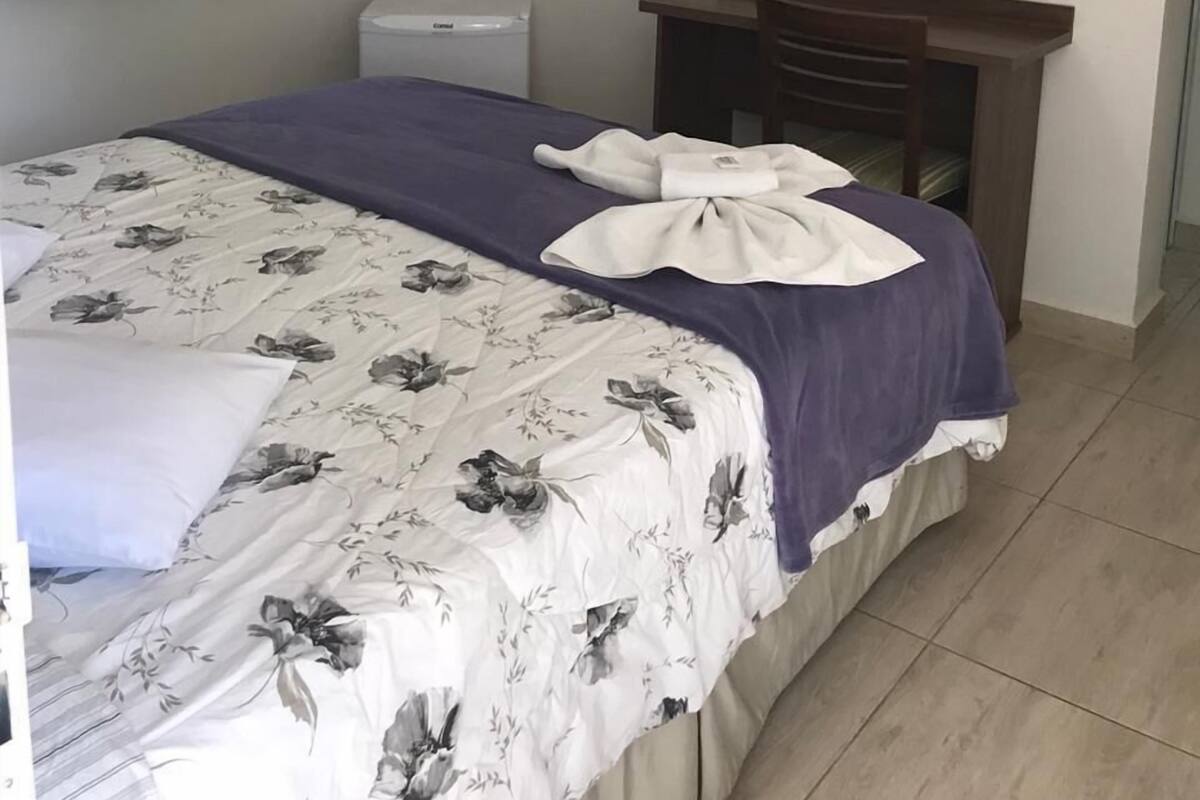 A bedroom with a bed, a flat-screen TV mounted on the wall, a desk, and a chair.