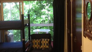 A room with a bed, a chair with a patterned cushion, a small table, and a view of greenery outside. - Palermo Soho Hostel (Buenos Aires)