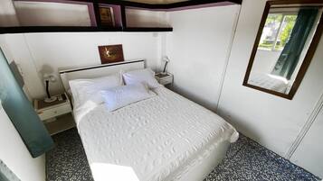 A neatly made bed with white linens, a bedside table with a lamp, and a wall-mounted air conditioner.
