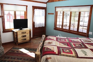 Un dormitorio con una cama, un aparador, un televisor y dos ventanas con cortinas.