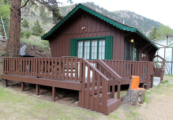 A wooden cabin with a green roof, a deck, and a staircase leading to the entrance. - Fawn Valley Inn: 157 (Estes Park)