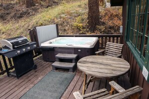 A hot tub and grill on a wooden deck with a table and benches. - Fawn Valley Inn: 157 (Estes Park)