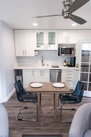 A modern kitchen with white cabinets, a microwave, a stainless steel dishwasher, and a ceiling fan.