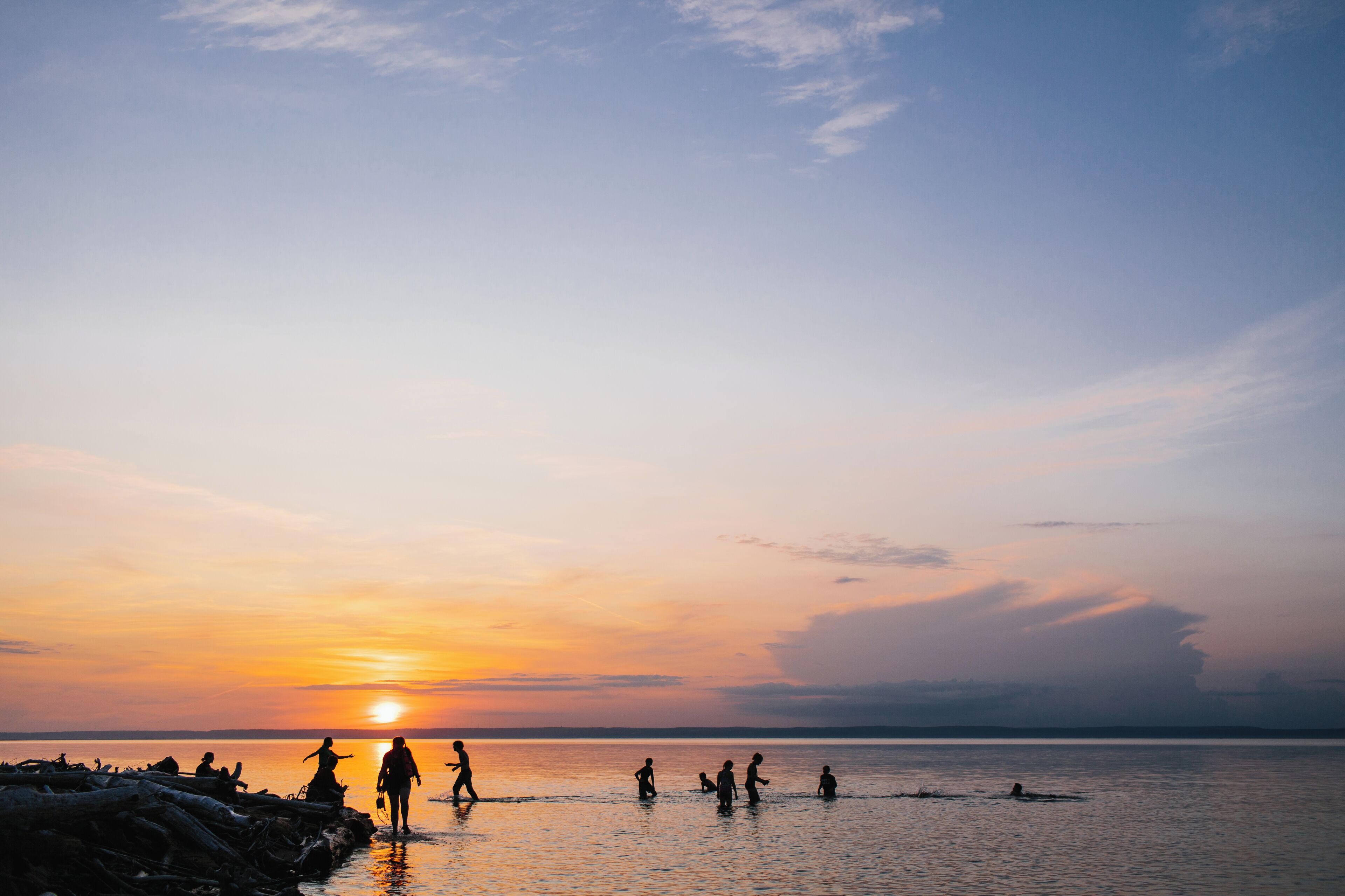 A sunset over a calm body of water with silhouettes of people enjoying the view.