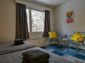 A room with two beds, a window with curtains, a radiator, a wall-mounted macrame decoration, and a blue patterned rug. - Nature Hotel (Northern Lights, Ruka, Kitka Lake) (Kuusamo)