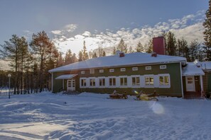 A green house with a snow-covered roof and a chimney, surrounded by trees and snow. - Nature Hotel (Northern Lights, Ruka, Kitka Lake) (Kuusamo)