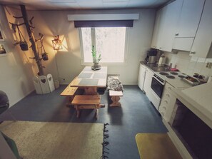 A compact kitchen with a dining table, benches, a small refrigerator, and a stove. - Nature Hotel (Northern Lights, Ruka, Kitka Lake) (Kuusamo)