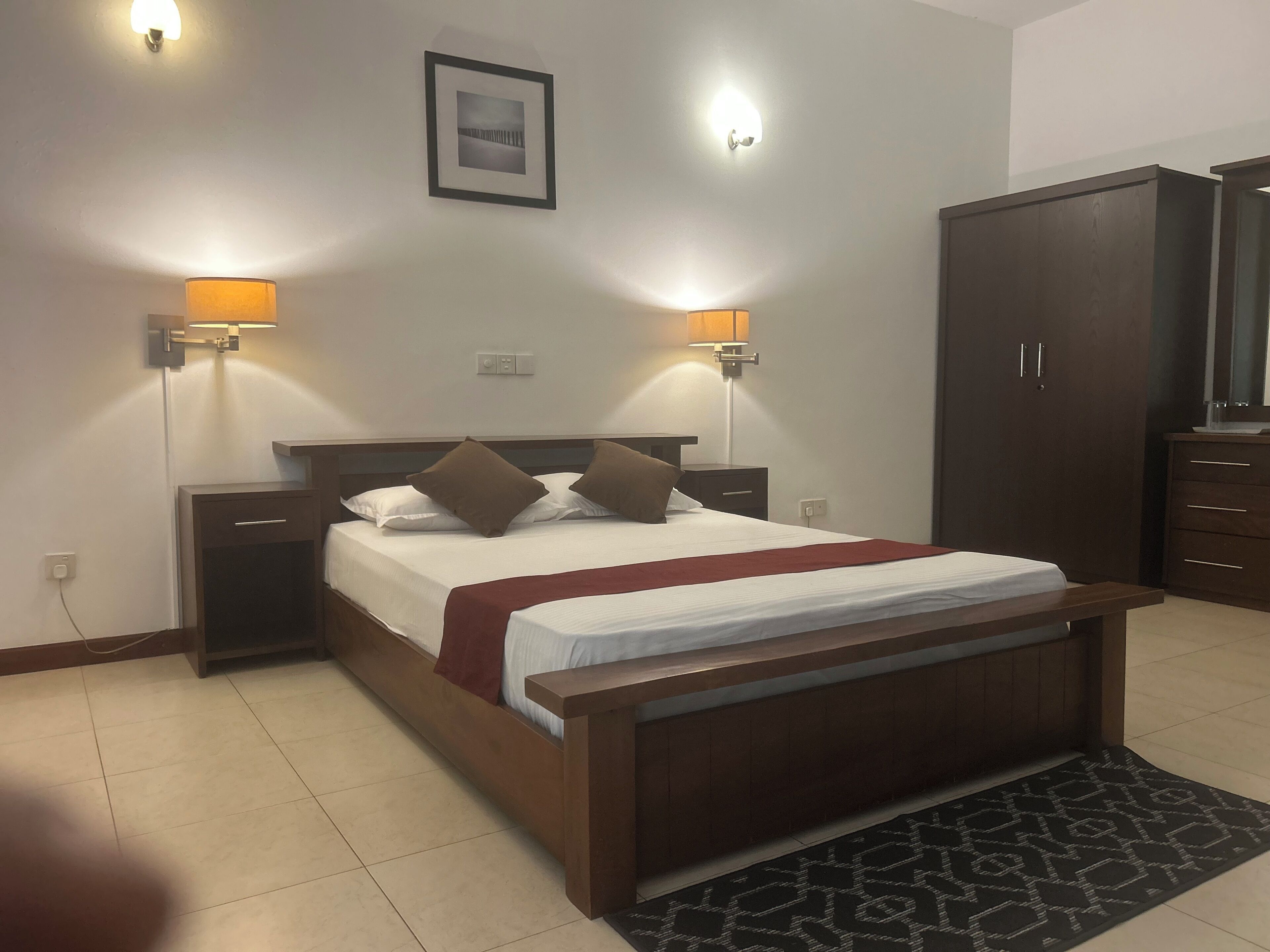 A hotel room with a bed, bedside lamps, a wardrobe, and a framed picture on the wall.