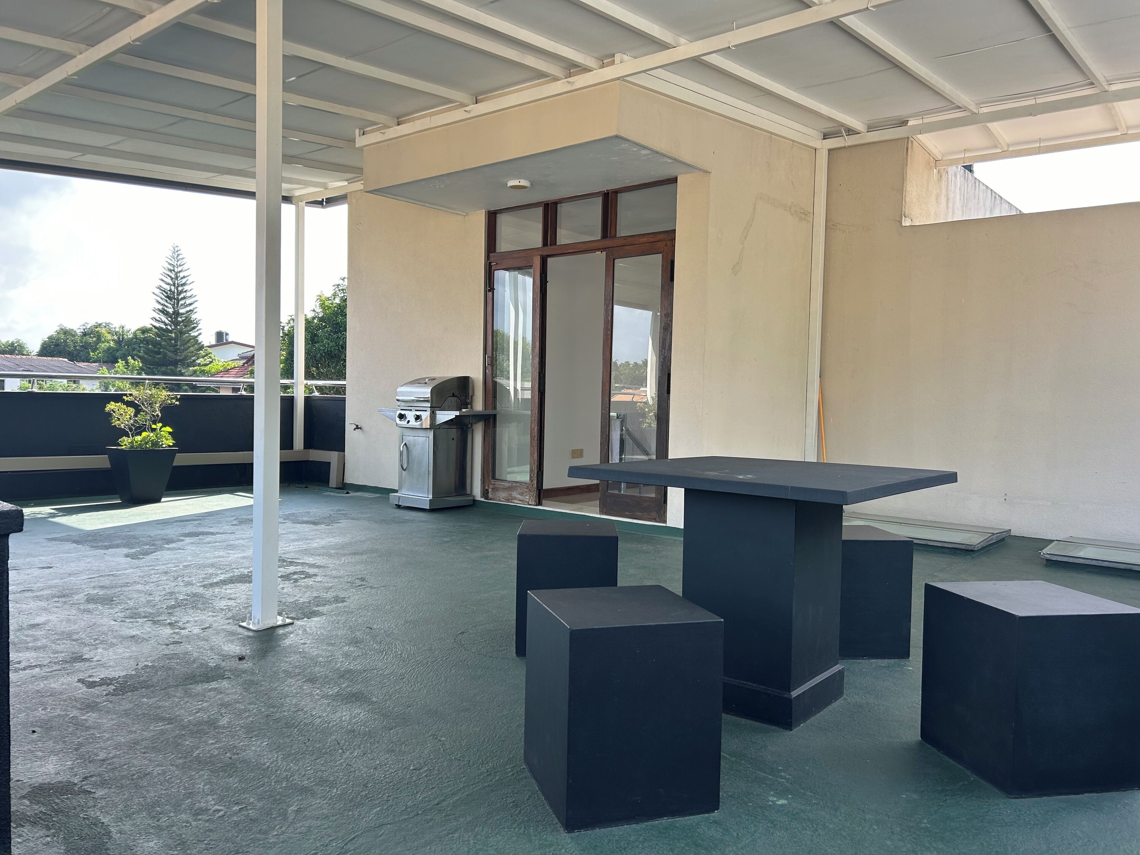 A covered outdoor area with a barbecue grill, a table with chairs, and a potted plant.