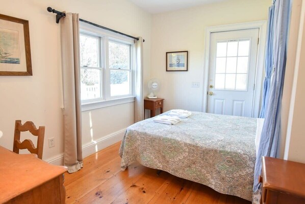 A bedroom with a bed, a chair, a small table, a window, and a door. - Waterfront Fun at this Huge Family Estate! (Eastham)