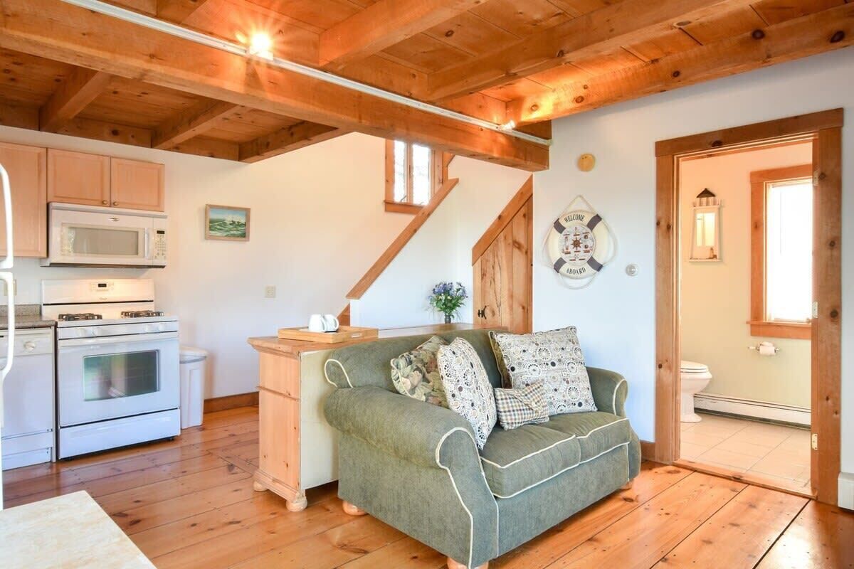 A cozy kitchen with wooden beams, a green sofa with patterned cushions, and a wooden staircase.