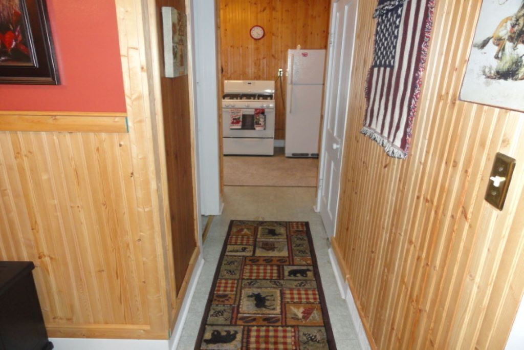 Un pasillo con paredes de madera, un tapete estampado, un refrigerador y un reloj en la pared.