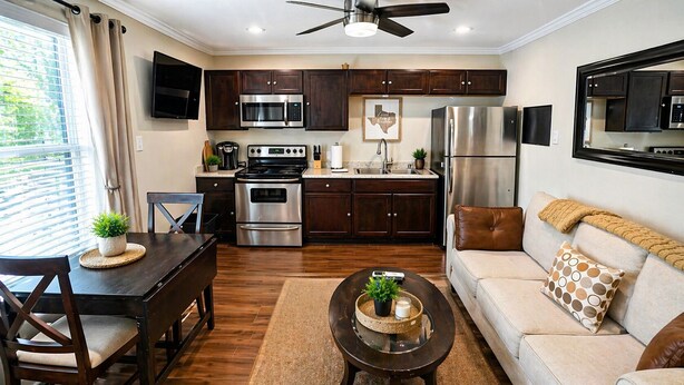 A modern kitchen with dark wood cabinets, stainless steel appliances, and a dining area with a wooden table and chairs. - Modern 1BR Retreat Full Kitchen Walkable Free Parking Apt B (Houston)