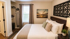 A bedroom with a bed, a nightstand, a lamp, a painting, a window with curtains, a ceiling fan, and a closet with hanging items. - Modern 1BR Retreat Full Kitchen Walkable Free Parking Apt B (Houston)