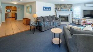 A living room with a fireplace, a television, and a kitchen in the background. - Short drive of just over 1 mile to Scarborough State Beach (Narragansett)