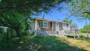 A two-story house with a porch, surrounded by trees and a grassy yard. - Short drive of just over 1 mile to Scarborough State Beach (Narragansett)