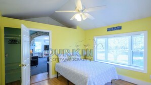 A bedroom with a bed, a ceiling fan, a window with blinds, and a door leading to another room. - Short drive of just over 1 mile to Scarborough State Beach (Narragansett)
